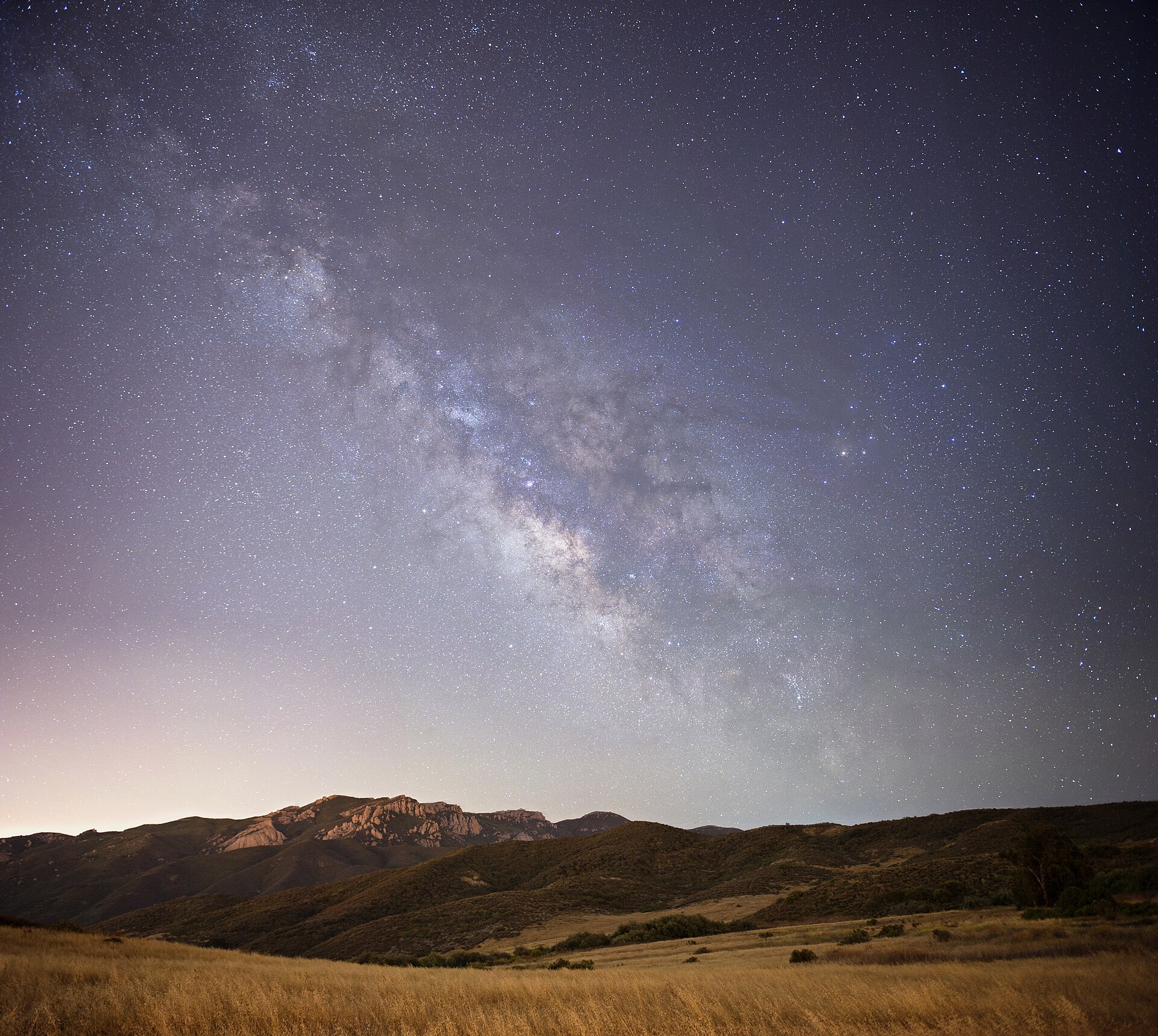 The Milky Way arching over a dark mountain horizon